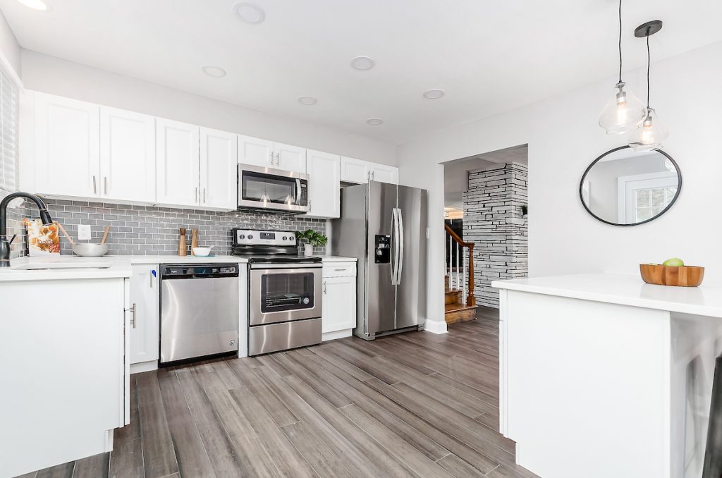 Revitalizing Neighborhoods, One House At A Time 6 A kitchen with a small mirror, stainless steel appliances, and nice flooring.