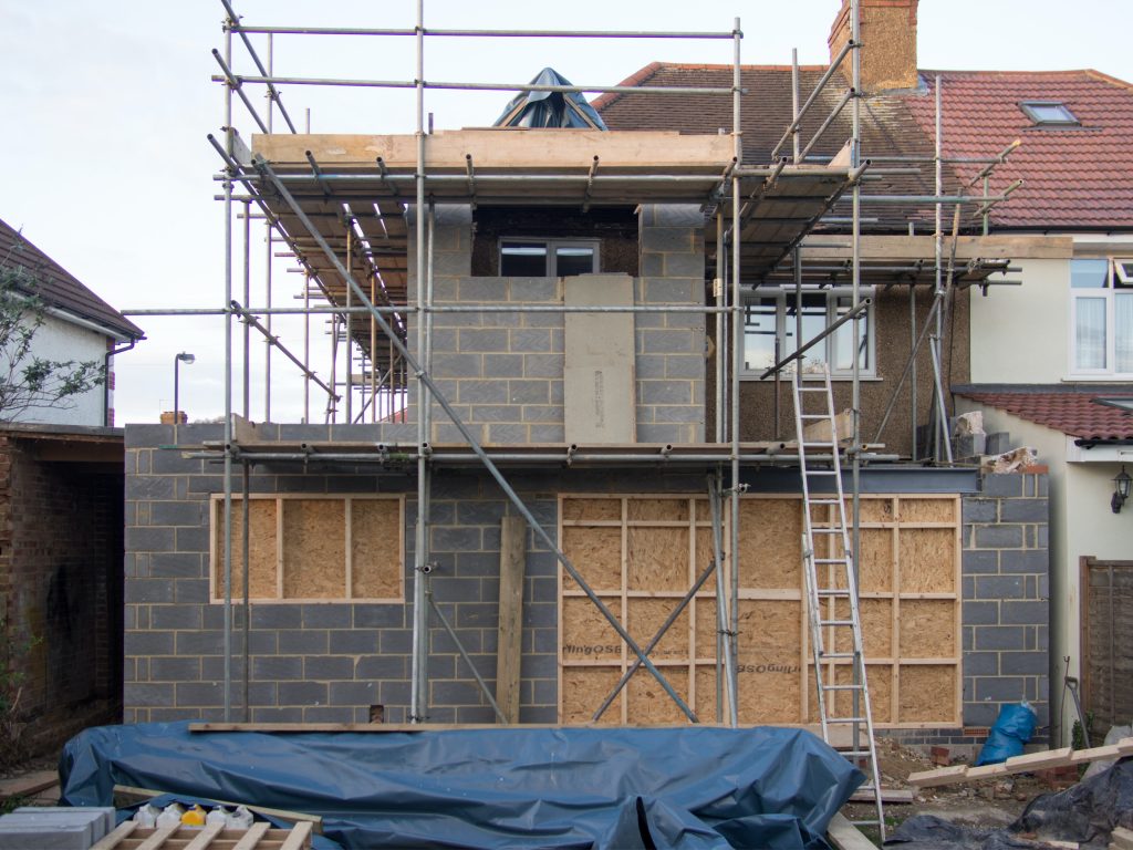 6 Great Ways to Lower Your Home Building Cost 3 Scaffolding and a blue tarp around a a house that is being built.