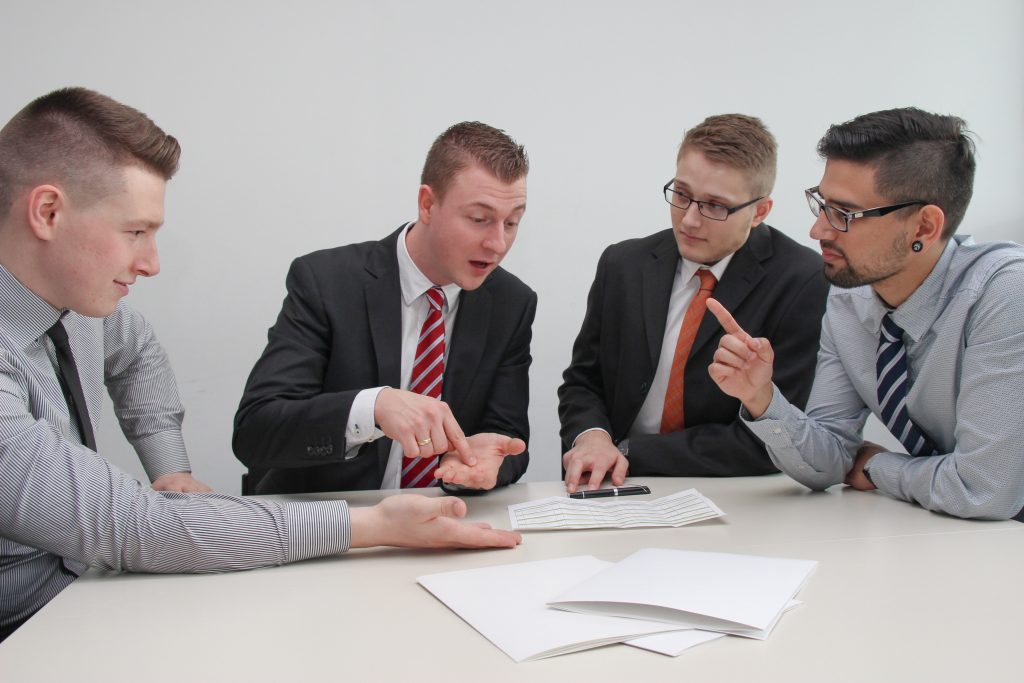 What Does a Title Company Do? 3 What does a title company do? It makes closing your home easier and safer as demonstrated by these four young men in business clothes and ties signing contracts on an eggshell white table.