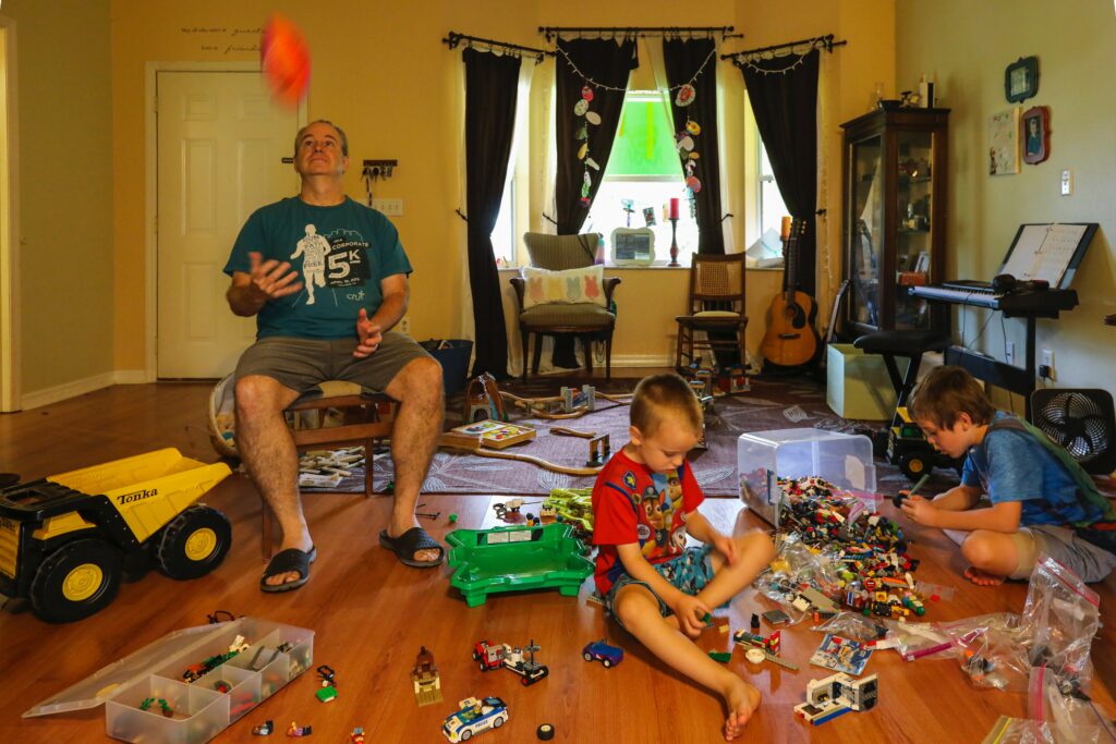 How to Prepare for a Move: Your 2021 Moving Checklist 2 Two children and a man haven't learned how to prepare for a move as they sit playing with toys in a messy room.